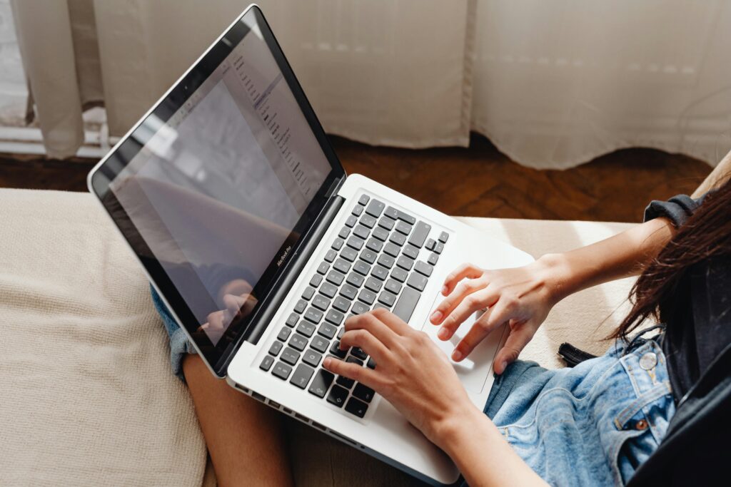 A person typing on a MacBook Pro laptop while seated on a couch