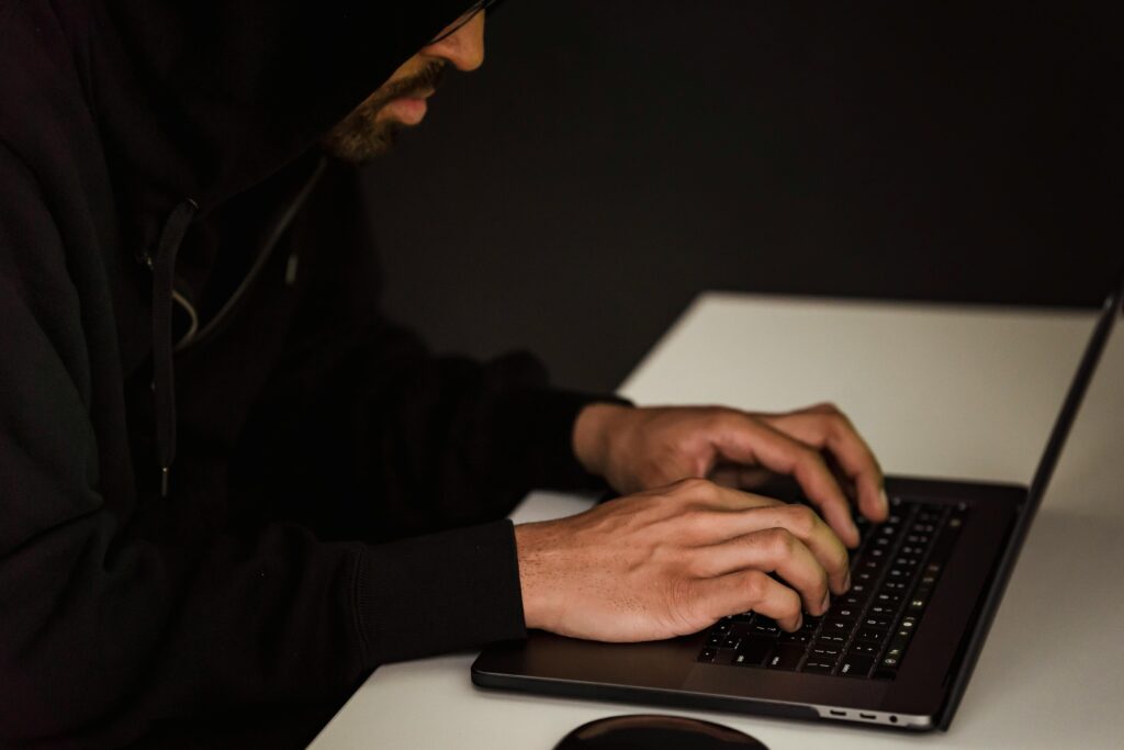 A hooded figure typing on a laptop in the dark representing a ransomware attack threat
